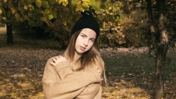 Jeune fille souriant à la caméra sous les feuilles tombantes dans le parc d'automne. — Video