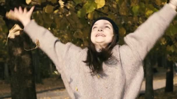 Drăguţă şi fericită fată cu pălărie care aruncă frunze de toamnă în parc. Încet. — Videoclip de stoc