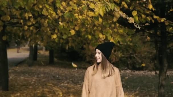 Ευτυχισμένο κορίτσι χαμογελά στην κάμερα κάτω από την πτώση φύλλα φθινόπωρο στο πάρκο — Αρχείο Βίντεο