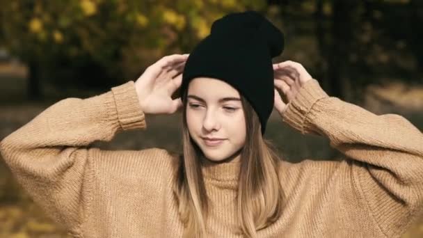 Όμορφο κορίτσι με καπέλο ποζάρει με χαμόγελο στο πρόσωπο στην κάμερα στο ηλιόλουστο πάρκο του φθινοπώρου — Αρχείο Βίντεο