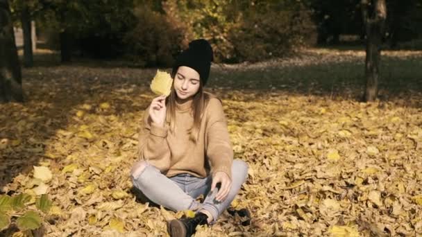 Jeune fille pose avec feuille d'automne à la caméra dans le parc. Doucement. — Video