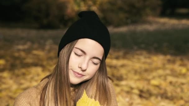Νεαρή έφηβη ποζάρει με φθινοπωρινό φύλλο στην κάμερα του πάρκου. Αργά. — Αρχείο Βίντεο