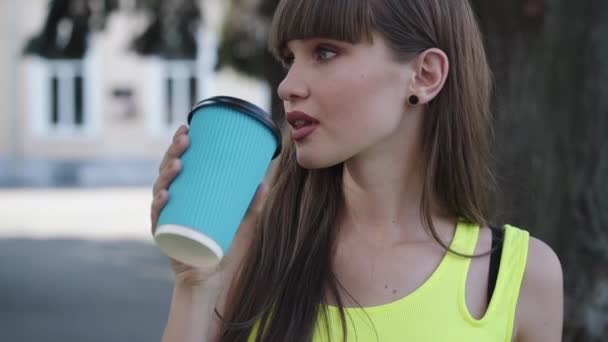 Stijlvol meisje drinkt een glas koffie en glimlacht opzij op straat — Stockvideo