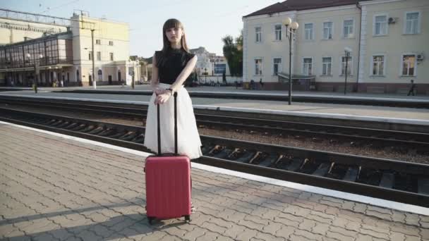 Elegante Dame steht bei sonnigem Wetter mit Koffer in Pose auf Bahnsteig — Stockvideo