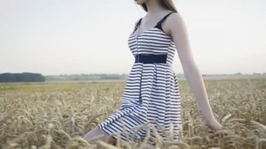 Zarif bayan buğday tarlasında yürüyor ve kameraya tutkulu bir şekilde bakıyor.