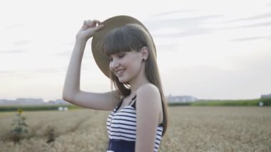 Tutkulu bayan şapkasıyla poz veriyor ve buğday tarlasında kameraya gülüyor.