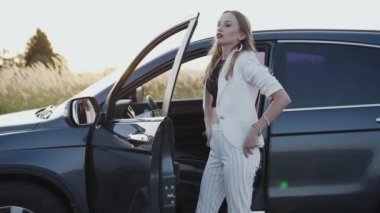 Arabadaki kız saçlarını düzeltir, ellerini cebine sokar ve gülümser.