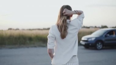 Beyaz elbiseli kadın saçını düzeltir ve şehir dışına doğru yürür.