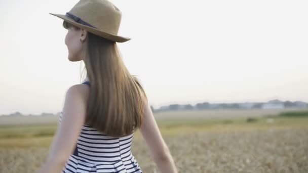 Jong, stijlvol meisje met hoed en jurk glimlacht en poseert zachtjes in tarweveld — Stockvideo