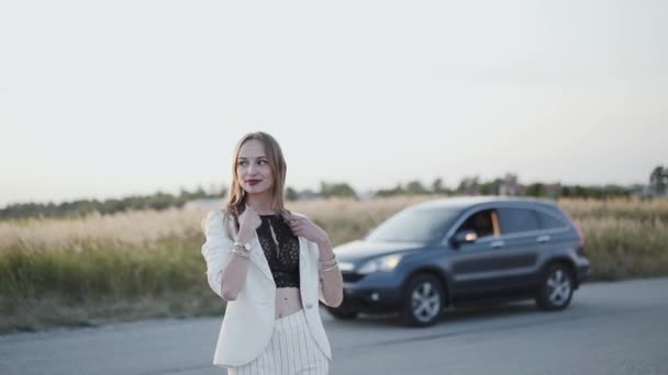 Menina bonita fica na estrada para fora da cidade, olha para o lado e sorri — Vídeo de Stock