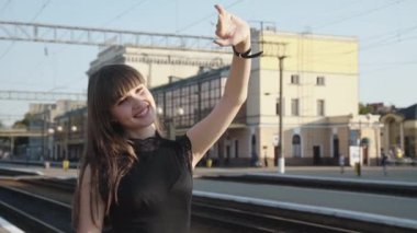 Zarif bayan elinde bavuluyla peronda duruyor ve güneş ışınlarına uzanıyor.