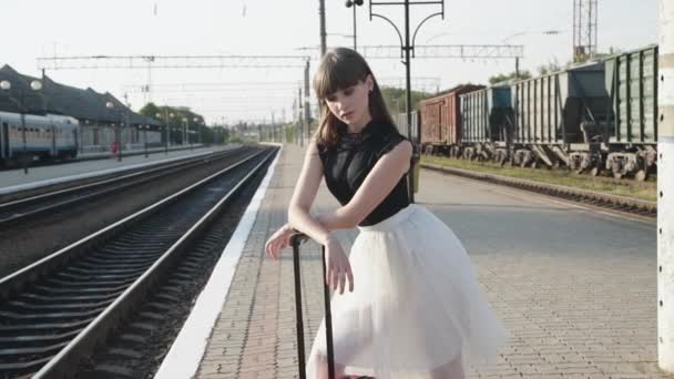 Modelo atractivo en vestido blanco y negro posa con maleta roja en la plataforma — Vídeo de stock