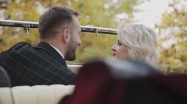 Romantik çift eski arabalarında hafif bir gülümsemeyle flört ediyor.
