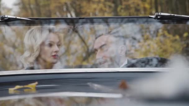 森の中のレトロな車の中で小さな話をして素敵なカップル。フロントガラスからの眺め — ストック動画