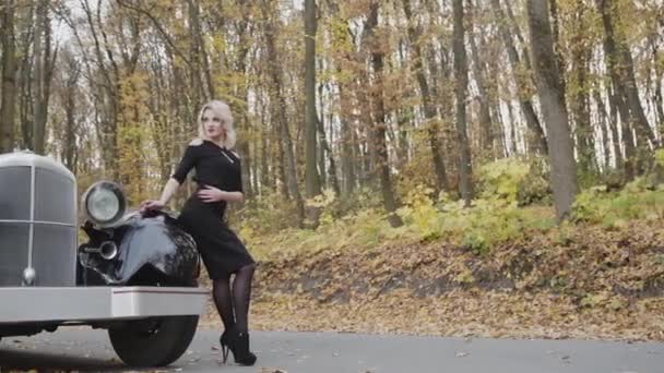 Portrét sexy blondýny v černých šatech lehce pózuje na retro kabriolet — Stock video