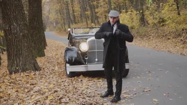 Porträtt av stilig gentleman korrigerar sin jacka i höstparken vid retrobilen — Stockvideo