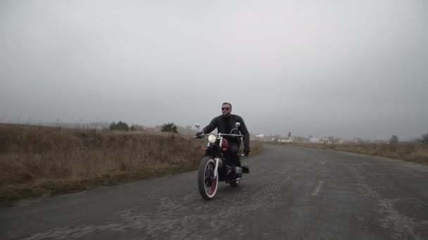 Νεαρός μοτοσικλετιστής οδηγεί στο δρόμο κοντά σε άγριο πεδίο έξω από την πόλη — Αρχείο Βίντεο