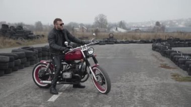 Motosikletli bir motosikletlinin portresi. Lastiklere bakıyor.