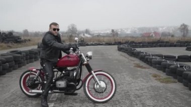 Motosiklete binmiş, lastiklerin yanına bakan vahşi bir adamın portresi.
