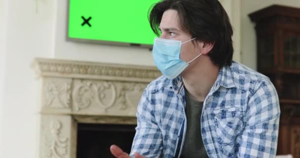 Сумний чоловік в масці ізольований вдома, божевільний на телевізійній плазмі з зеленим екраном — стокове відео