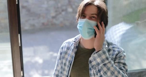 Άντρας με μάσκα αναπνέει καθαρό αέρα κοντά στο παράθυρο και μιλάει στο τηλέφωνο στο σπίτι — Αρχείο Βίντεο