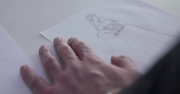 Bovenaanzicht van mannelijke ontwerpers hand tekent een trouwjurk schets op papier — Stockvideo