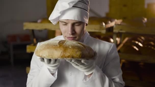 Vista próxima do padeiro em uniforme fareja pão fresco e tem prazer — Vídeo de Stock