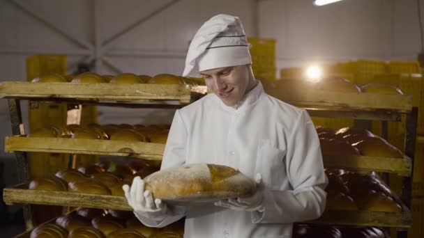 Piekarz w mundurze pokazujący duży okrągły bochenek chleba z obrazem uśmiechu przed kamerą — Wideo stockowe