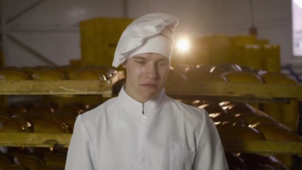 Young baker in uniform raises large loaf of round bread at face level and smiles — Stock Video