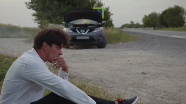 El hombre se sienta de la hierba y espera el servicio de coche — Vídeo de stock