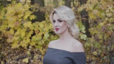 Hoş bir bayanın portresi hafifçe gülümsüyor ve sonbahar parkında saç stilini düzeltiyor.