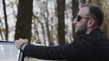 Acımasız adam parlak arabaya yaslandı kameraya döndü ve güneş gözlüğünü düzeltti.