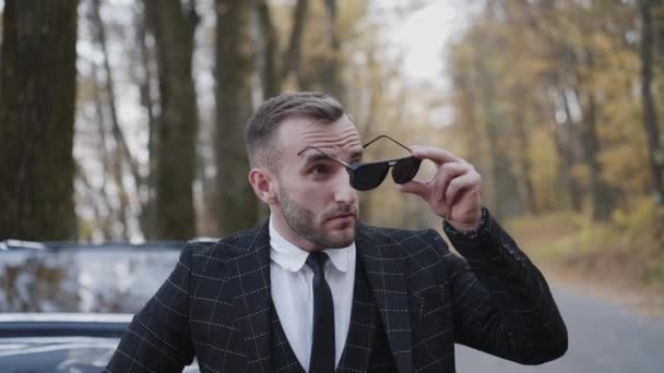 Guapo caballero de traje se para en coche retro y se pone gafas de sol — Vídeo de stock