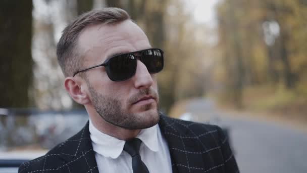 Portrét seriózního muže v slunečních brýlích a obleku stojí v retro autě — Stock video