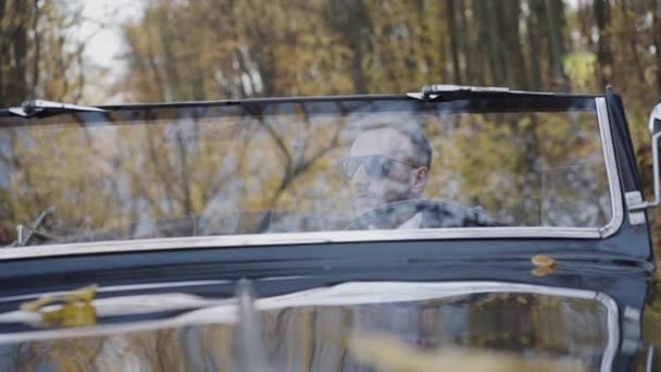Портрет через вітрове скло людина сидить за кермом глянцевого автомобіля — стокове відео
