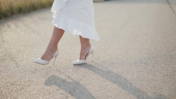 Pernas femininas em branco saia longa e sapatos poses passo a passo elegante na estrada — Vídeo de Stock