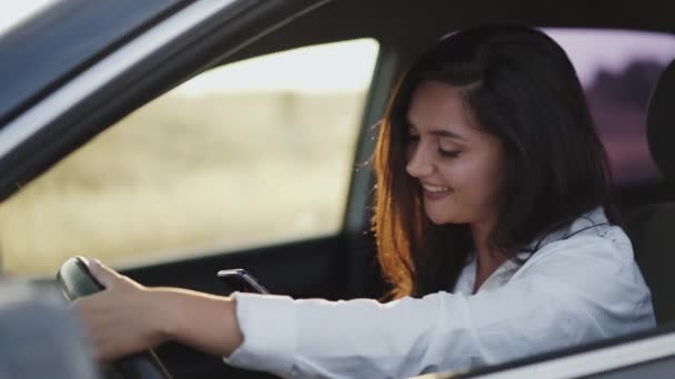 Menina feliz sorrindo ao digitar no smartphone no carro — Vídeo de Stock