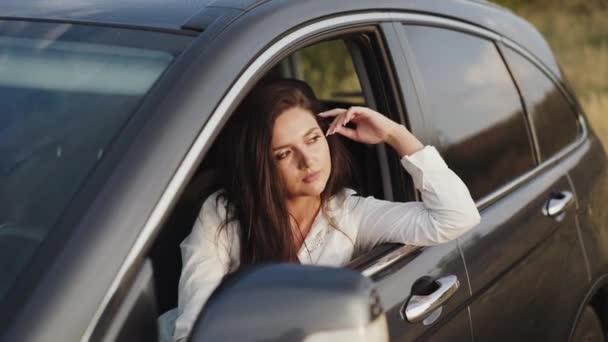 Chica bonita se asoma por la ventana del coche, mira hacia fuera y sonríe — Vídeo de stock