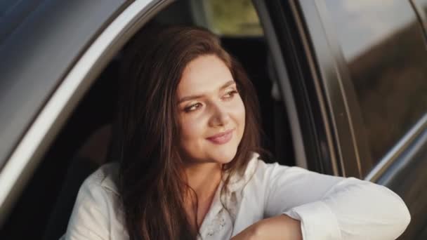 Chica bonita se asoma por la ventana del coche, mira hacia fuera y sonríe a la cámara — Vídeo de stock