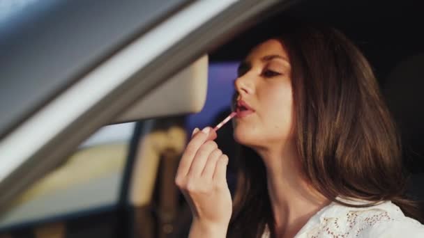 View of pretty long-haired girl applying lipstick at car front mirror — Stock Video