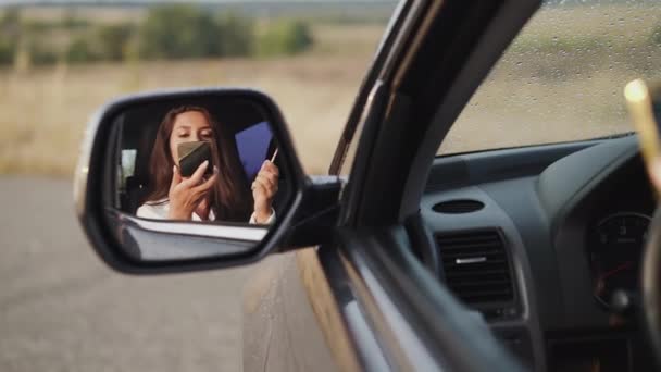 Відбиття жінки в дзеркалі заднього виду автомобіля, яка наносить блиск для губ — стокове відео