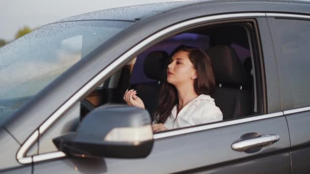 Brünette trägt Wimperntusche auf den Außenspiegel des Autos auf und lächelt in die Kamera — Stockvideo