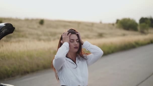 Vista de la mujer nerviosa desconcertante en el capó del coche fuera de la ciudad — Vídeos de Stock