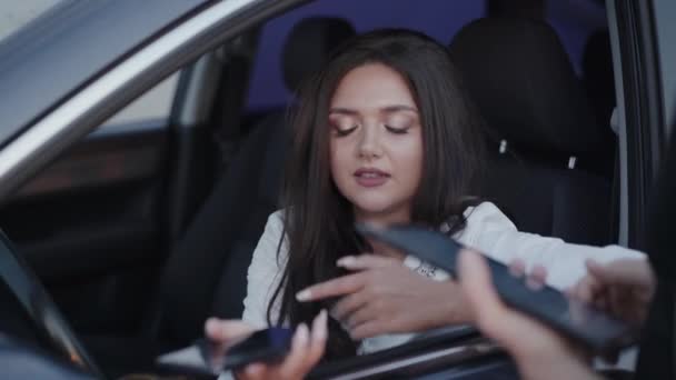 Запутавшаяся девушка в машине со смартфоном разговаривает с кем-то с гаджетом и улыбками — стоковое видео