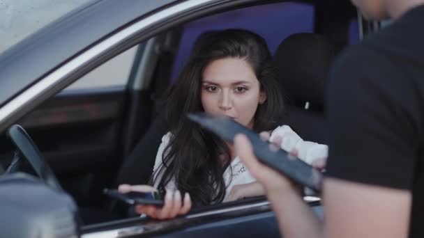 Эмоциональная женщина в машине разговаривает с офицером, они используют гаджеты и улыбаются — стоковое видео