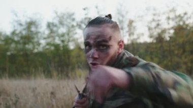 Kurum bantlı dövüşçü bir bıçak sallıyor ve kameraya dışarıda vuruyor.