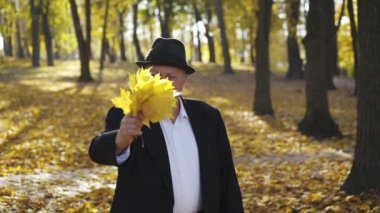 Takım elbise ve şapka giymiş son sınıf öğrencisi kameraya akçaağaç buketi bırakıyor.