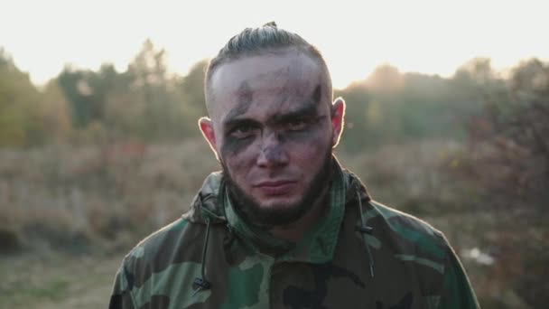 Portrét vojáka s rozmazanými sazemi na obličeji při pohledu na kameru při západu slunce — Stock video