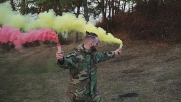 Soldado em uniforme de camuflagem brinca com fumaça rosa e amarela — Vídeo de Stock