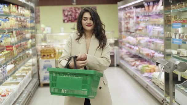 Magabiztos boldog nő egy kosárral a kezében mosolyog a kamera a szupermarketben — Stock videók